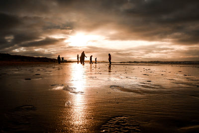 Silhouette people on beach against sky during sunset