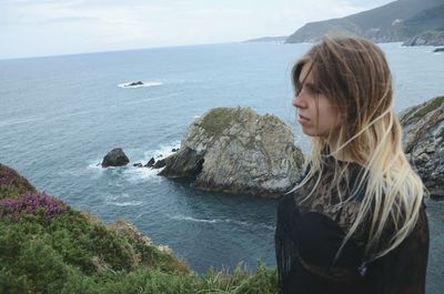 Woman standing on cliff by sea against sky