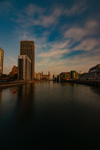 Scenic view of river by buildings against sky during sunset