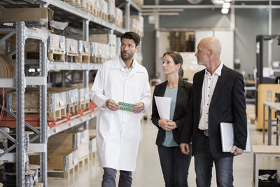 Male engineer and business people looking at storage shelves in industry