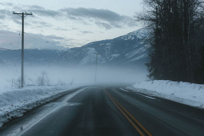 Road amidst snowcapped mountains against sky during winter