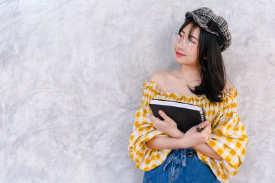 Young woman holding camera while standing against wall