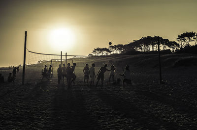 Silhouette people playing soccer on field against sky during sunset