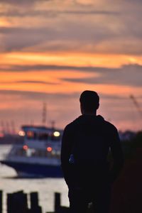 Silhouette man standing at harbor against orange sky