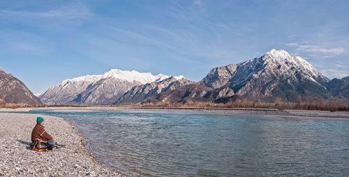 Man sitting at riverbank during winter