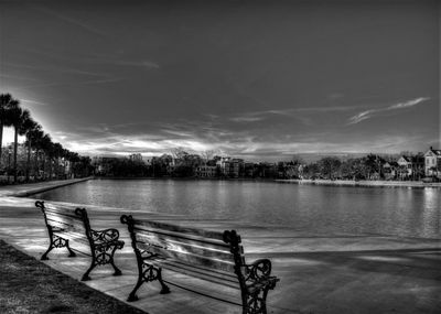 Empty bench by lake against sky