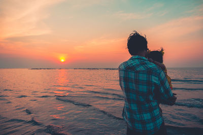 Rear view of man looking at sea against sky during sunset