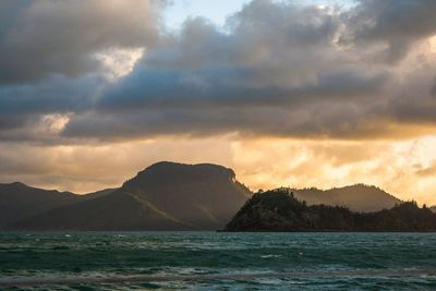 Scenic view of lake and mountains against cloudy sky at sunset