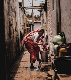 Side view full length of mature woman washing cloth at alley