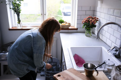 Woman arranging plates in cabinet while standing by kitchen counter