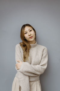 Portrait of young woman wearing sweater while standing against gray background