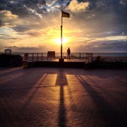 Silhouette people on street by sea against sky during sunset