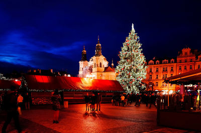 People celebrating christmas by illuminated buildings at night