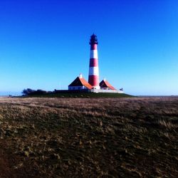 Lighthouse on field against clear blue sky