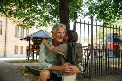 Smiling man embracing grandson outside school gate