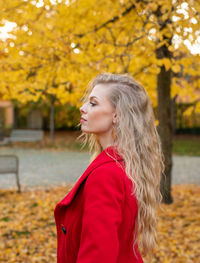 Woman looking away while standing on tree during autumn