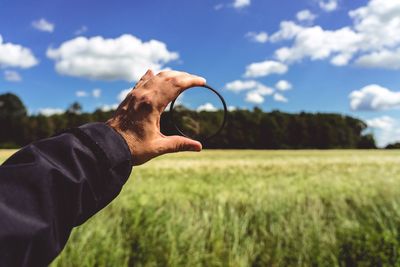 Cropped hand of person holding magnifying glass against sky