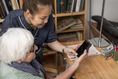 Home carer helping senior woman to use cell phone