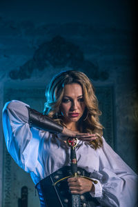 Woman in costume holding sword standing against door of abandoned building at night