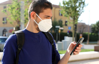 Man wearing mask using mobile phone while standing outdoors