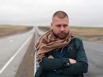 Mid adult man with arms crossed standing on road against sky