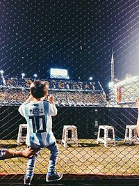 Rear view of man standing on soccer field at night