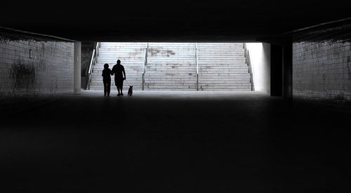 Silhouette man and woman walking with dog in tunnel