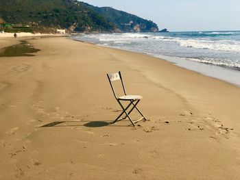 Empty chairs on beach against sky