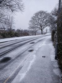 Road amidst bare trees against sky during winter