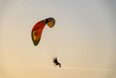 Low angle view of people paragliding against clear sky