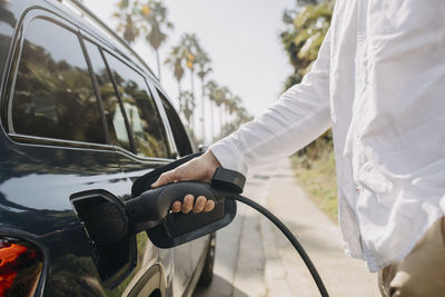 Man plugging charging cord into electric car on road at station