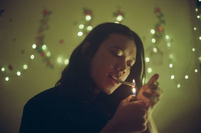 Young woman igniting cigarette against illuminated lighting equipment