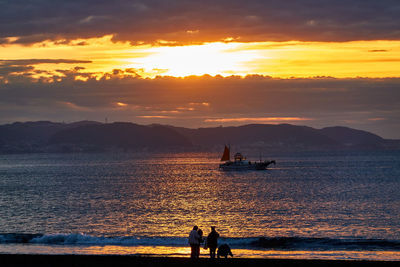 People on sea against sky during sunset
