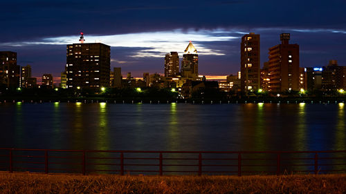 Illuminated buildings by river against sky at night