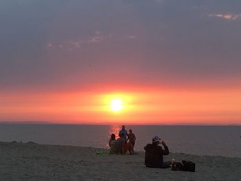 People sitting on beach against sky during sunset