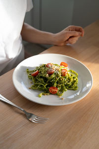 Woman made pasta with sauce pesto for lunch sitting on table at home. homemade italian cuisine.