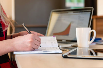 Cropped hand of woman writing in diary on desk at office