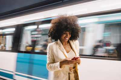 Smiling woman using smart phone in front of moving subway train