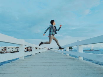 Full length of man jumping on footbridge over sea against sky