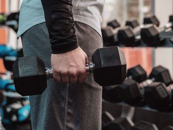 Midsection of man lifting dumbbell while standing in gym