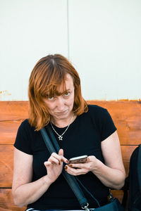 Portrait of woman using mobile phone against wall