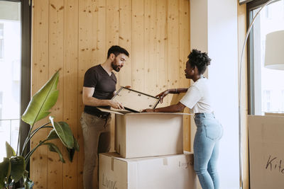 Couple talking to each other while removing frame from cardboard box at new home