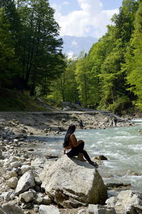 Man on rock in forest against sky