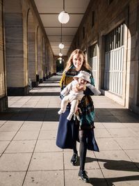 Portrait of smiling mother carrying daughter while walking in corridor