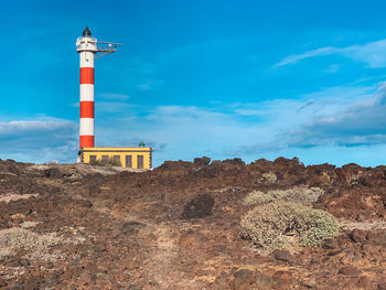 Lighthouse on rock by building against sky