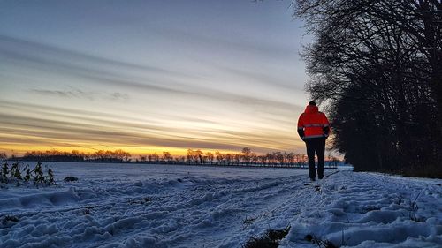 Rear view of man on snow covered field against sky during sunset