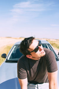 Smiling man wearing sunglasses while sitting on car against sky