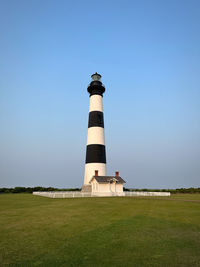 Lighthouse by sea against clear blue sky