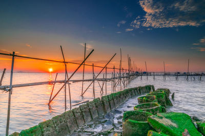 Wooden posts in sea against sky during sunset