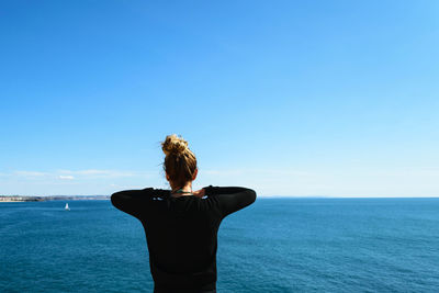 Rear view of woman standing by sea against clear blue sky